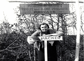 A women leans on a sign that says “Packer” while standing under a sign that reads “Morning Glory Trout and Game Preserve: Private”.